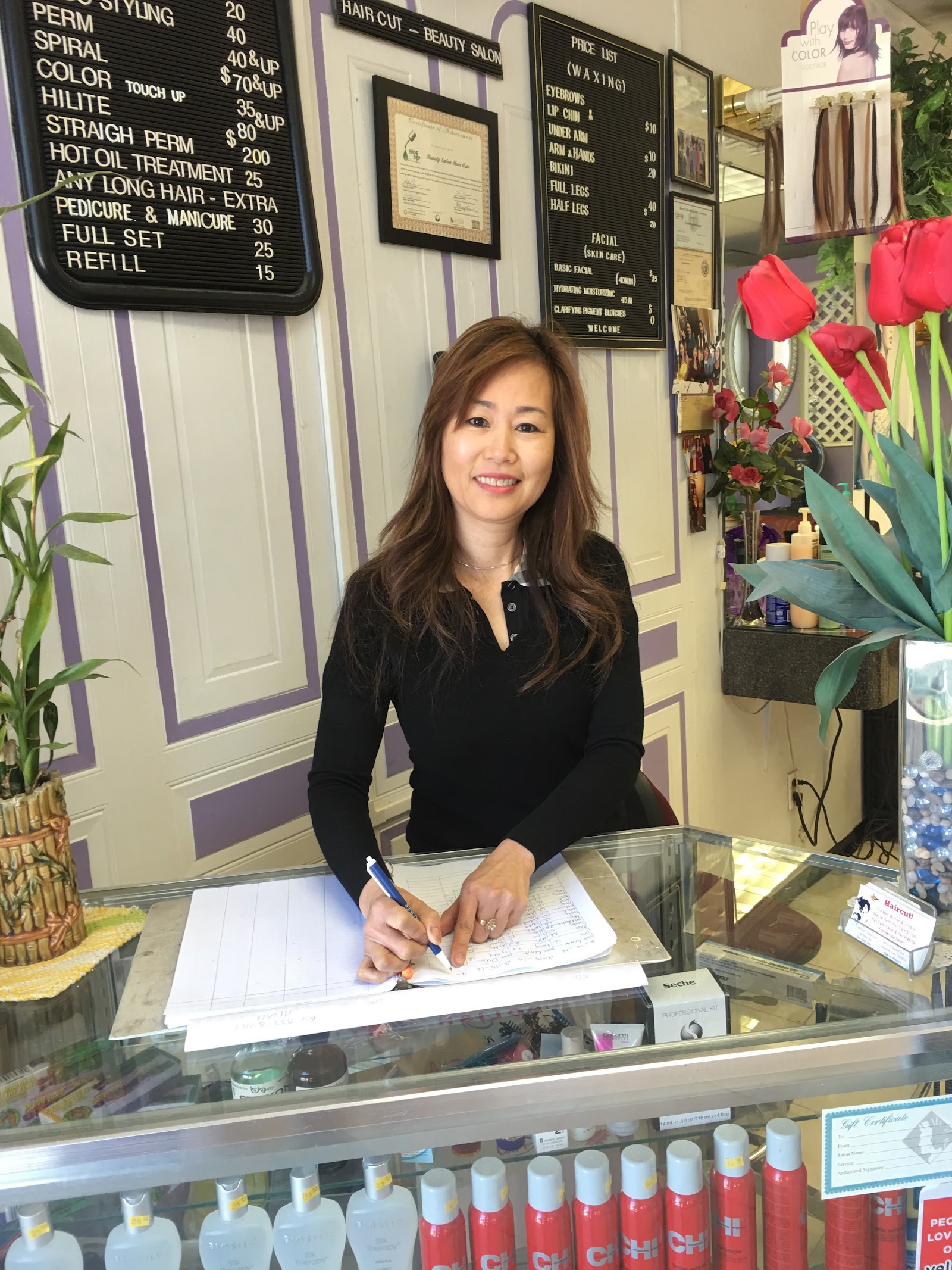 A stylist at the front desk of Haircut Beauty Salon, with the chalkboard service menu visible on the wall behind her.