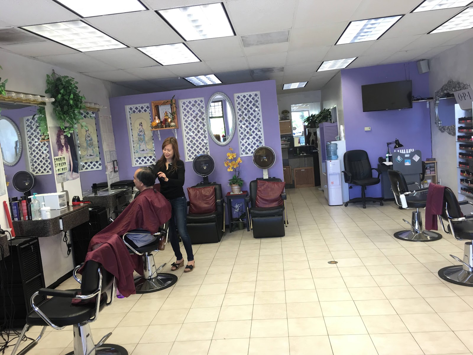 Inside the salon: lavender walls with white lattice mirror frames, burgundy styling chairs, a stylist trimming a man's hair.