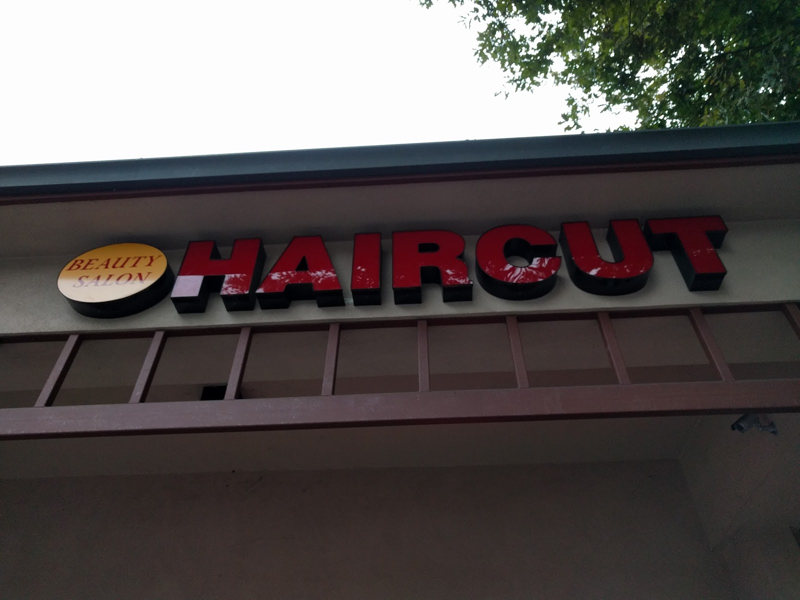 The red HAIRCUT sign with a yellow BEAUTY SALON badge above the storefront.